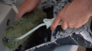 Banyoda boya silindiri temizleyen bir adam var..