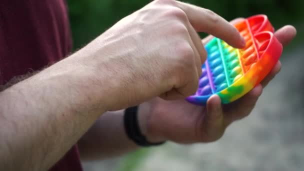Άνθρωπος που παίζει με το παιχνίδι pop αυτό απλό λακκάκι κάθεται στο πάρκο — Αρχείο Βίντεο