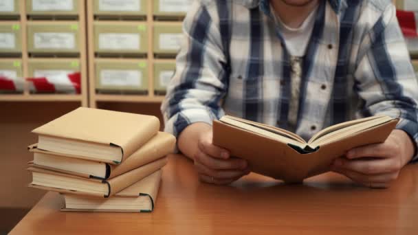 Un hombre lee un libro en la biblioteca sentado a la mesa — Vídeo de stock