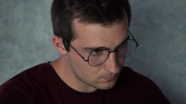 Gözlüklü bir adam ofisinde otururken dizüstü bilgisayarda çalışıyor.