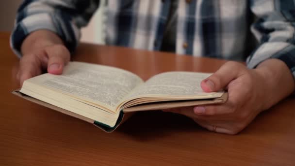 Een man die een boek leest terwijl hij aan een tafel zit — Stockvideo