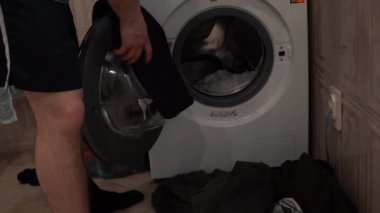 Bir adam kirli çamaşırları çamaşır makinesine atar..