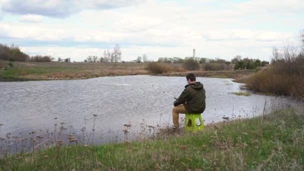Um homem pescando em uma lagoa sentado em uma cadeira — Vídeo de Stock