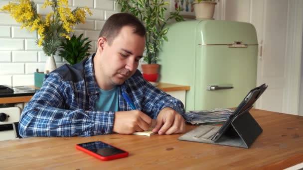 Ein Mann macht sich Notizen, während er in der Küche sitzt — Stockvideo