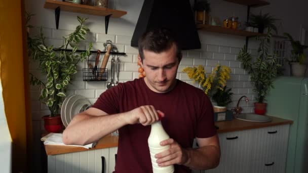 Человек пьет молоко стоя на кухне — стоковое видео