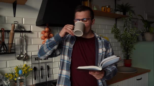 Ένας άντρας διαβάζει ένα βιβλίο στην κουζίνα πίνοντας τσάι. — Αρχείο Βίντεο