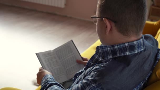 Egy szemüveges férfi könyvet olvas a kanapén. — Stock videók