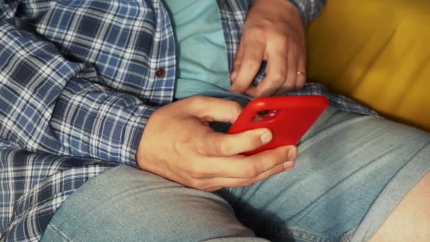En man som använder en röd telefon när han sitter på soffan — Stockvideo