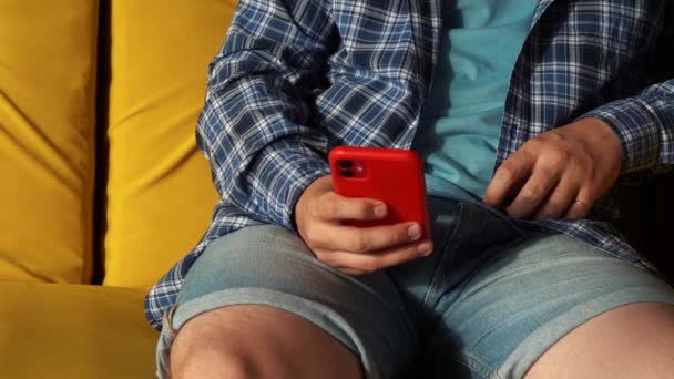 Un hombre usando un teléfono rojo mientras está sentado en el sofá — Vídeos de Stock