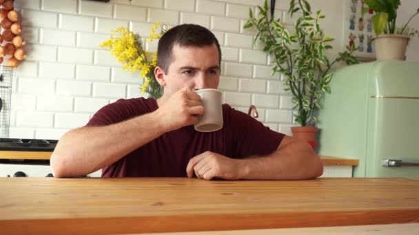Hombre bebiendo té de una taza sentada a la mesa en la cocina — Vídeo de stock