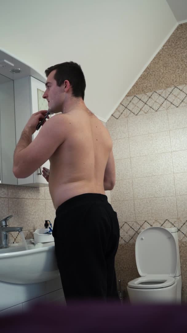 Muž se holí v koupelně. vertikální video — Stock video