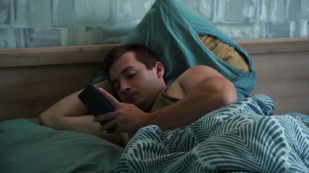 Мужчина пользуется телефоном, лежа в постели — стоковое видео