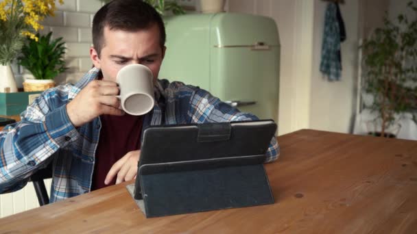 Hombre viendo una película en una tableta sentada en una mesa en la cocina — Vídeo de stock