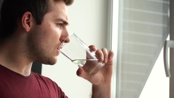 Человек пьет воду стоя у окна утром в комнате — стоковое видео
