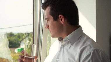 Beyaz gömlekli adam bardaktan su içiyor.