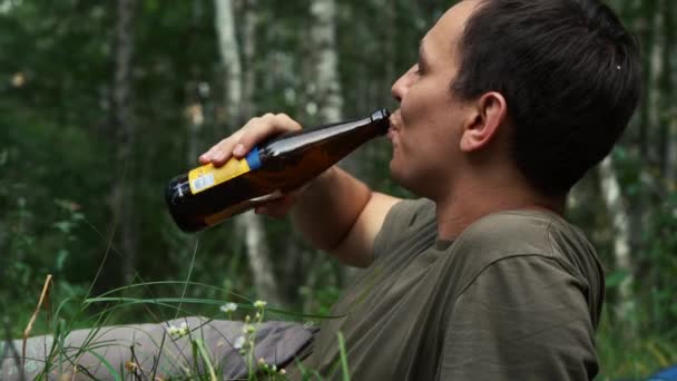 Muž pije pivo, zatímco sedí v lese u ohně — Stock video