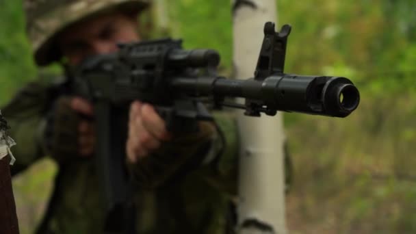 Soldat visé avec une mitrailleuse, regardant par derrière un arbre dans la forêt — Video