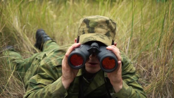 Soldado mirando a través de los prismáticos acostados en los arbustos — Vídeos de Stock