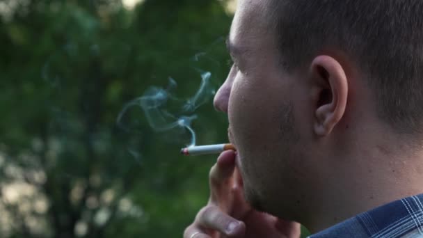 Человек курит сигарету, стоя спиной к камере — стоковое видео