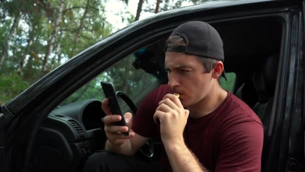 Homem fuma cigarros eletrônicos enquanto sentado no carro e usa o telefone — Vídeo de Stock