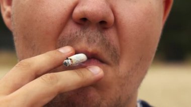 Sakallı adam sahilde sigara içiyor.