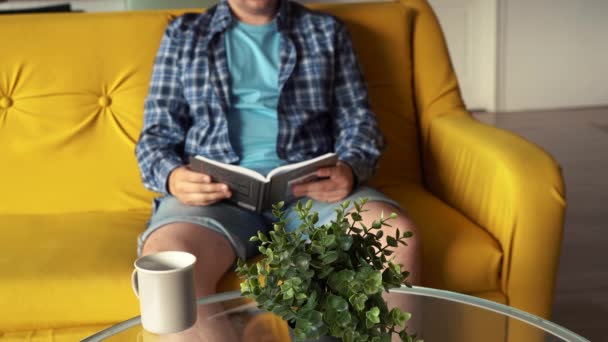 Un hombre leyendo un libro sentado en el sofá — Vídeo de stock