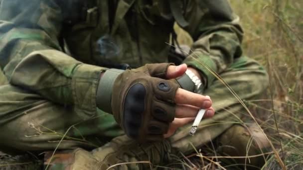 Man in uniform smokes a cigarette while sitting on the ground — Stock Video