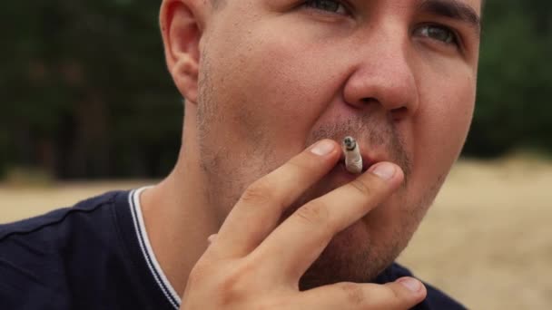 Skäggig man röker en cigarett på stranden — Stockvideo