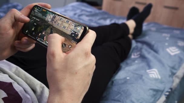 男はソファに寝そべって携帯電話で遊んでる。モスクワロシア2021年8月27日 — ストック動画