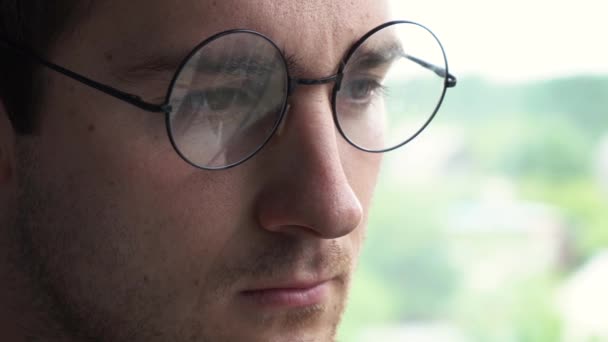 Człowiek w okrągłych okularach wygląda przez okno. Materiał 4k — Wideo stockowe