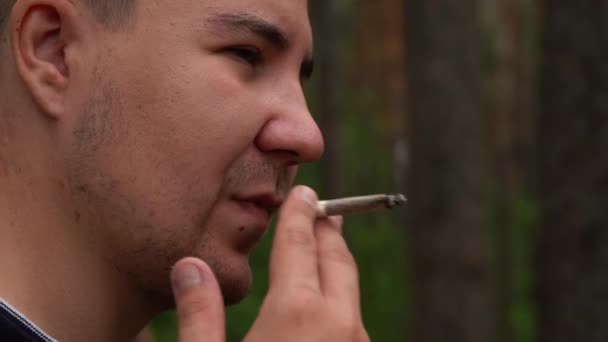 Hombre fuma un cigarrillo de pie en el bosque — Vídeos de Stock