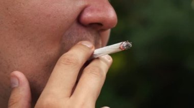 Bir adam bir yaz günü sokakta dikilirken sigara içer.