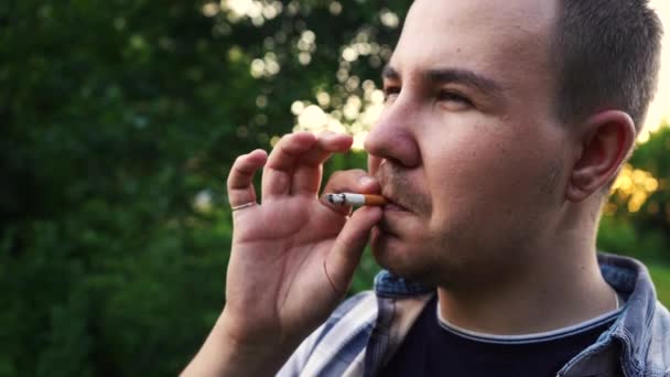 Hombre fuma un cigarrillo mientras está de pie con la espalda a la cámara — Vídeos de Stock