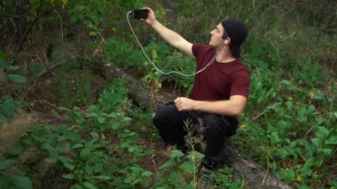 Bir adam ormanda devrilmiş bir ağaçta otururken video iletişimiyle iletişim kuruyor..