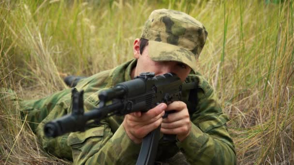 Voják míří z kalašnikovské útočné pušky, zatímco sedí v záloze. — Stock video