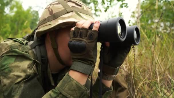 Soldado mirando a través de los prismáticos acostados en los arbustos — Vídeos de Stock