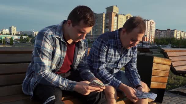 Két férfi megszámolja a pénzt és átöltözteti őket, miközben egy padon ülnek a parkban. — Stock videók