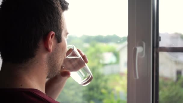 Uomo che beve un bicchiere d'acqua davanti alla finestra — Video Stock