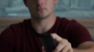 Adam televizyonun önünde otururken kumandayı kullanıyor.