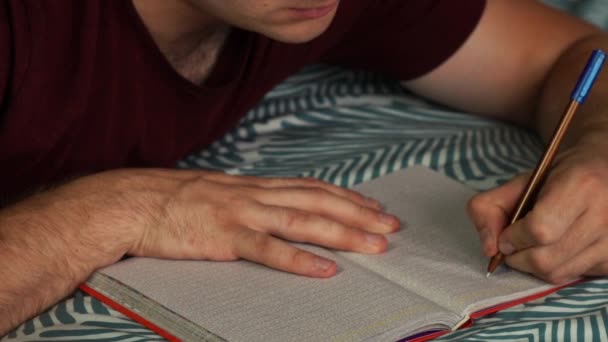 Egy férfi jegyzetel egy jegyzetfüzetbe, ami a kanapén fekszik. — Stock videók