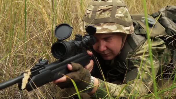 Francotirador masculino apuntando con un rifle de francotirador mientras está sentado en una emboscada. — Vídeos de Stock