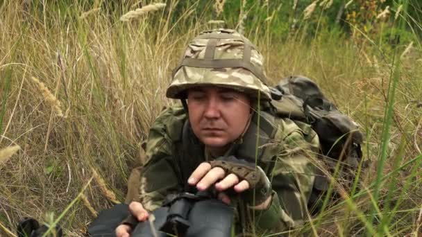 Man looks through binoculars, and then aims with a rifle from an ambush — Stock Video