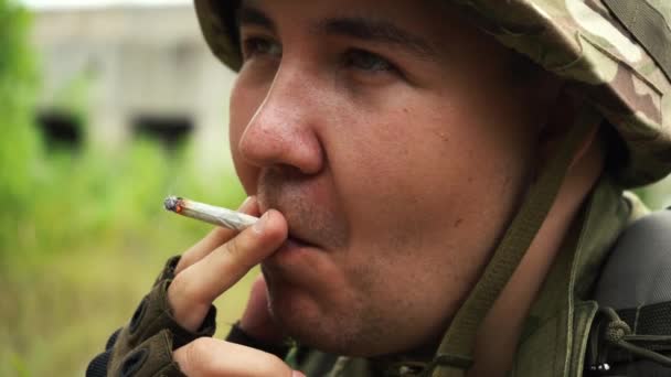 Muž v maskáčových uniformách kouří cigaretu na zastávce — Stock video