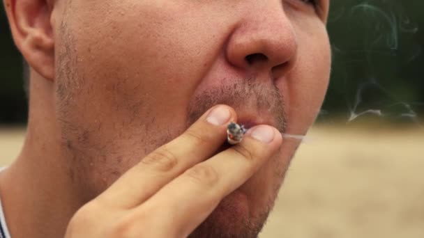 Hombre fumando cigarrillos de pie en la playa de cerca — Vídeo de stock