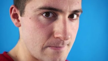 Adam mavi arka planda şüpheli bir şekilde kameraya bakıyor.