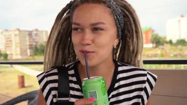 Jong meisje in dreadlocks drinkt limonade uit een blik — Stockvideo