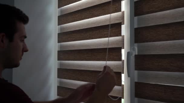 En man öppnar persiennerna i sitt rum på morgonen i gryningen — Stockvideo