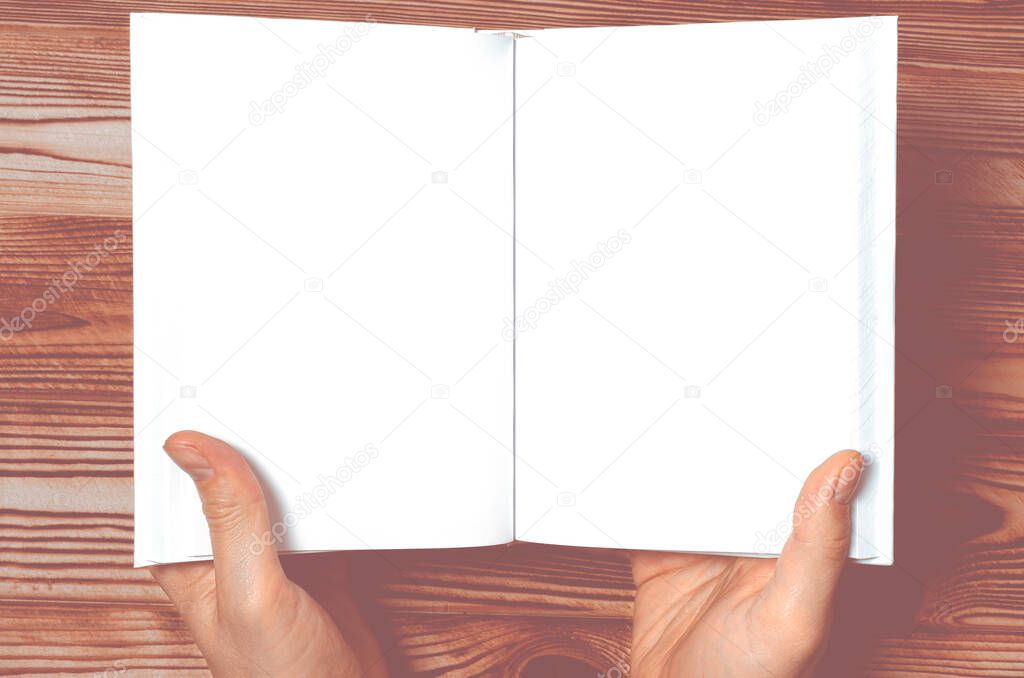 A mock-up of a white book with a place for text in the hands of a man on a wooden table