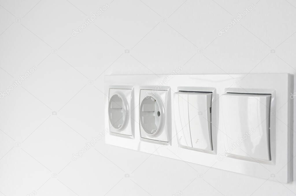 White plastic walk-through switches and sockets on a white wall. Repairs