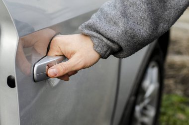 Sıcak giysili bir adamın eli gümüş renkli arabanın kapısını açar.